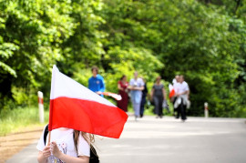 Dziecko z flagą na szosie. Flaga zasłania mu twarz. 